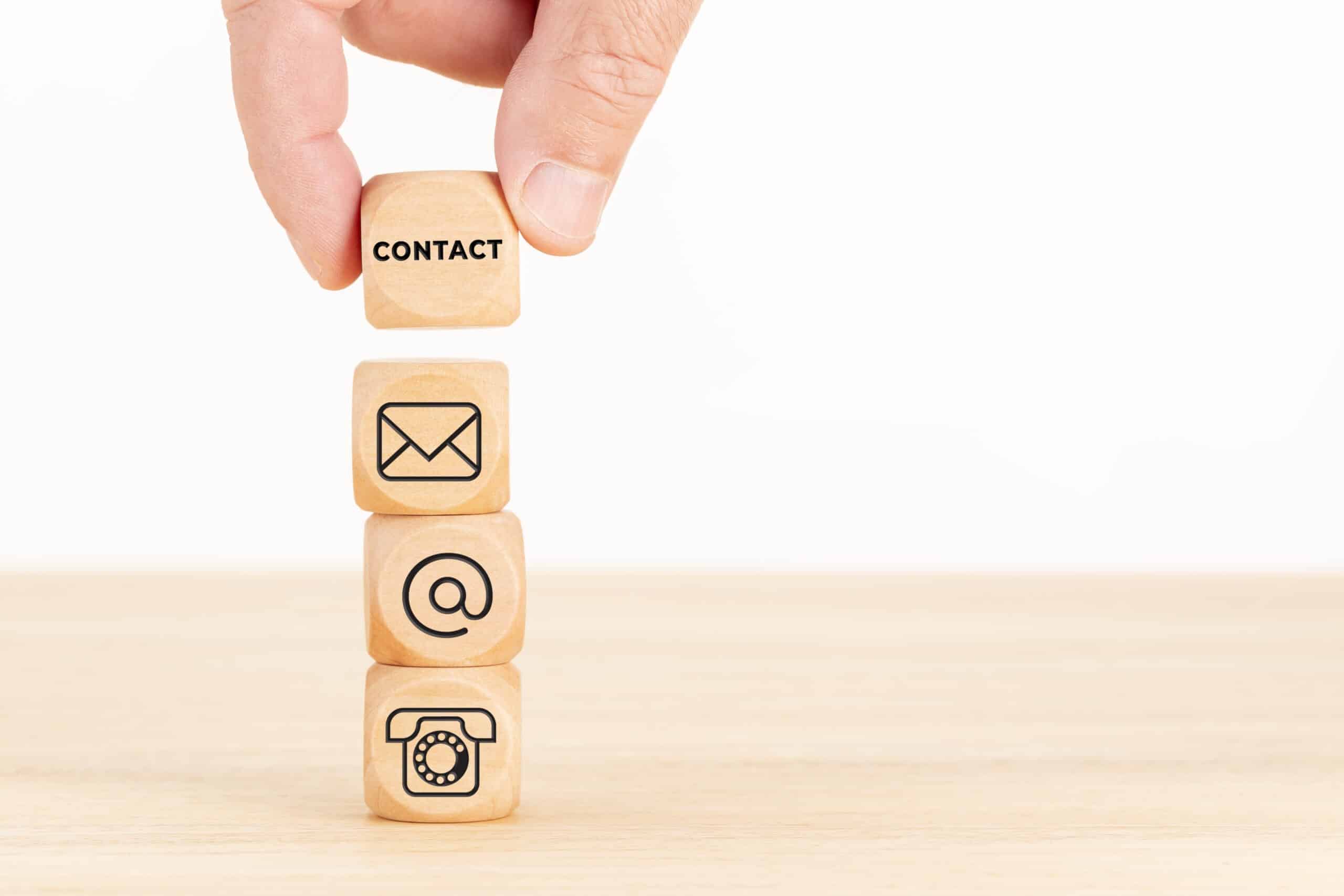 Contact us concept. Hand holding a wooden block with text and a pile of dices with communication icon
